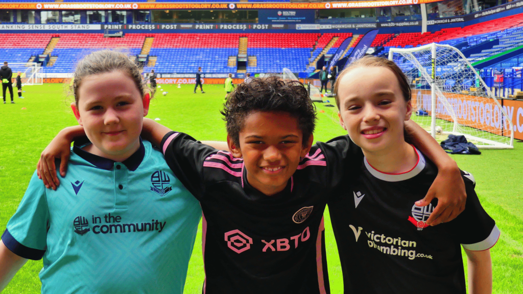 Close-up of three smiling kids posing together after football practice.