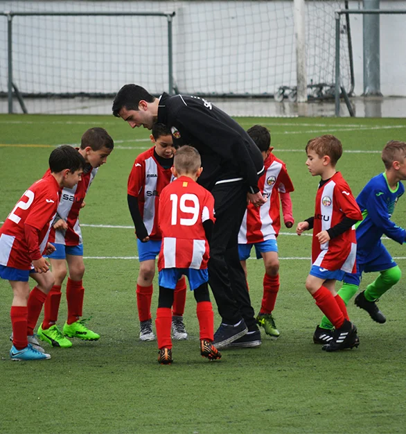 A coach guiding young players on a football field during training.