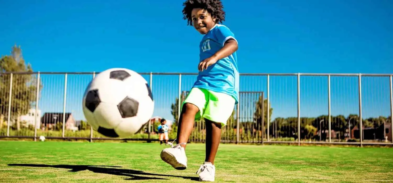 A boy kicking a ball and smiling to the fullest