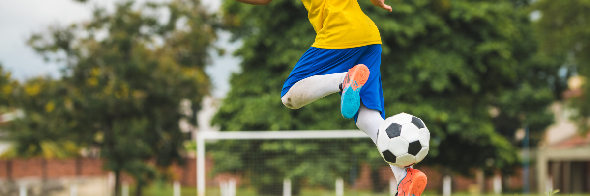 A young football player sets themself apart from competition by showing his unique ball control skills for his player profile, he is kicking the ball up from behind himself.