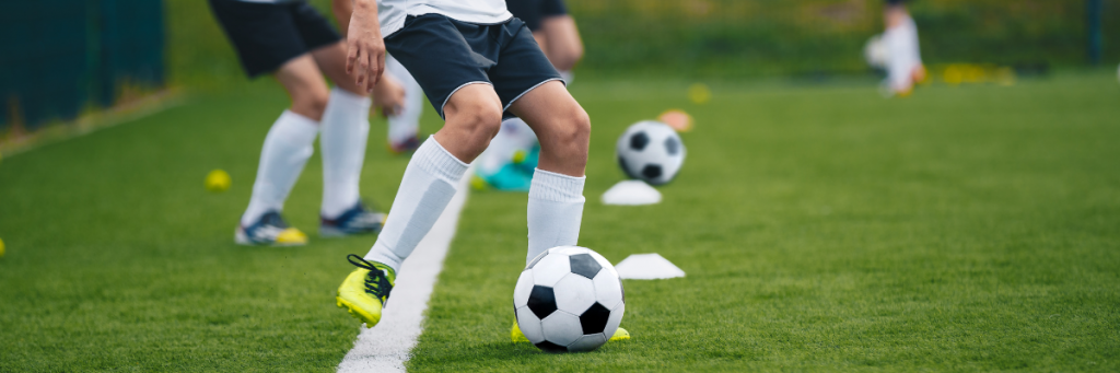 Football players are developing their skills for their player profile, they're practising their ball control skills with cones on the ground.