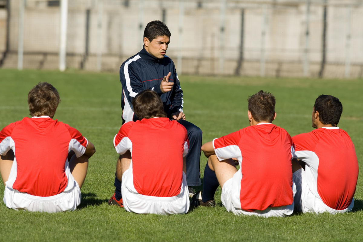 A football coach is talking to his team, he is training them on what it takes to get scouted.
