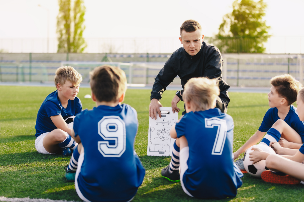 A coach is giving feedback to his players. It is important they take it onboard to appeal to Football Scouts Looking for Players.